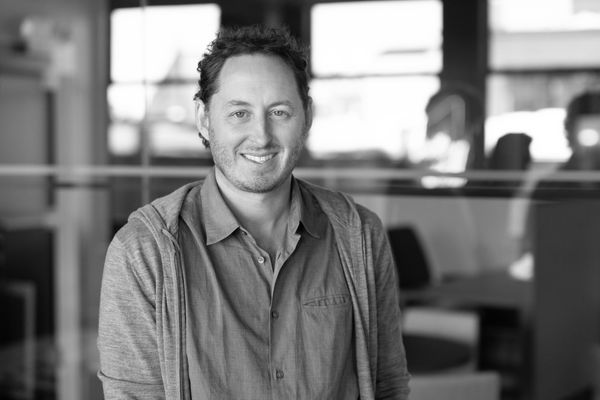 Smiling man in casual shirt and hoodie in a modern office setting.