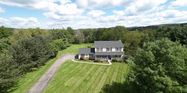 A two-story house surrounded by large green lawn and trees under a blue sky.