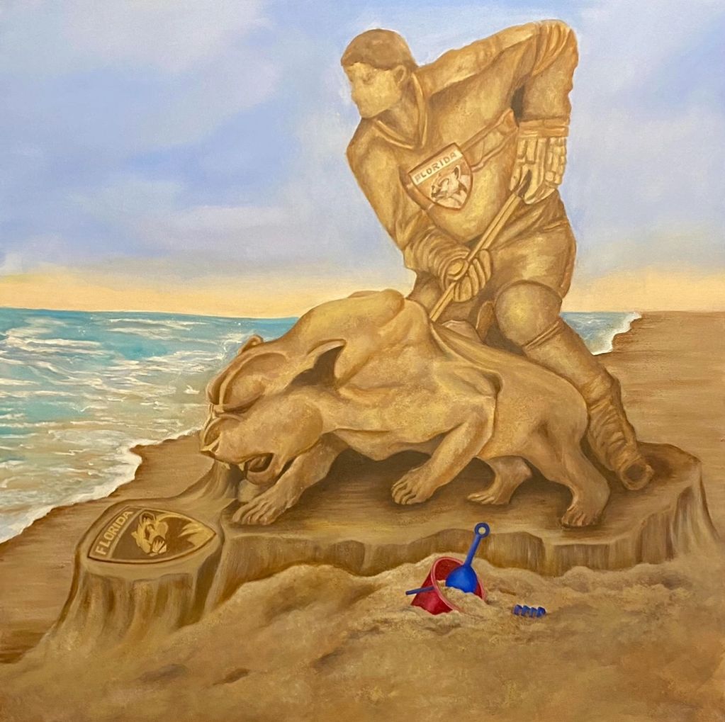 A sand sculpture of a hockey player and panther on a beach with a bucket and shovel.