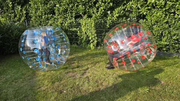 Two people inside transparent bubble balls playing on grass.