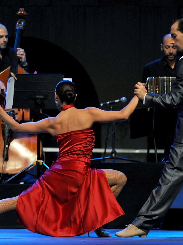 Couple performing a passionate tango dance with live musicians in the background.
