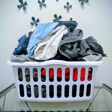 A laundry basket overflowing with clothes on a glass table.