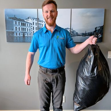 Man holding a large black garbage bag and smiling indoors.