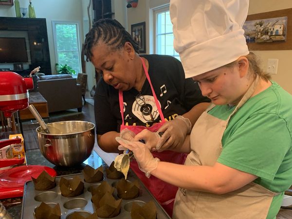 Zoe pours cupcake batter into baking sheet cups.