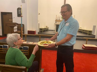 A man collects offering from a seated woman in a church.