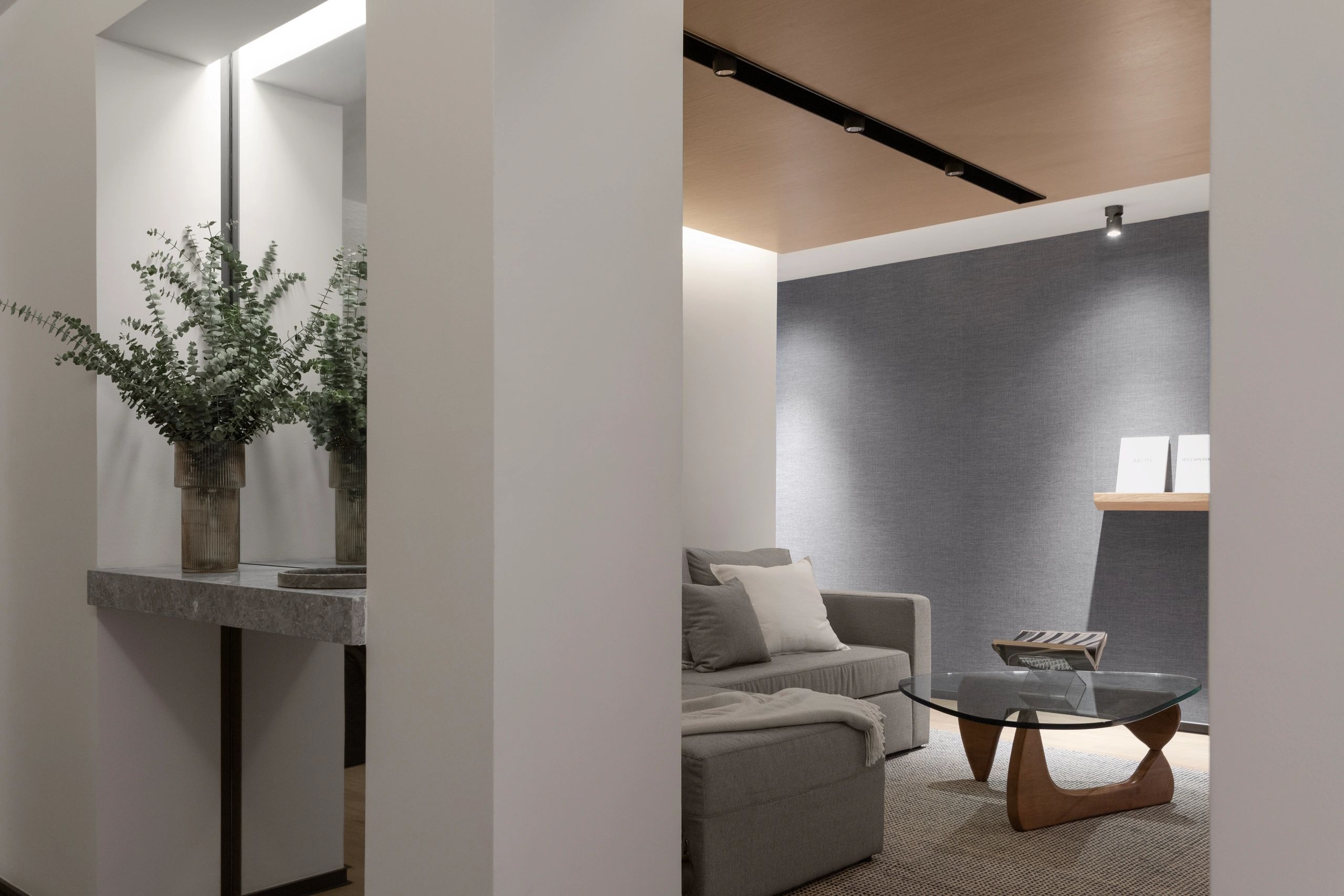 Sala moderna y minimalista con sofá gris y mesa de centro de vidrio.
