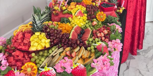 Colorful fruit display with flowers on tables draped in pink and red cloth.