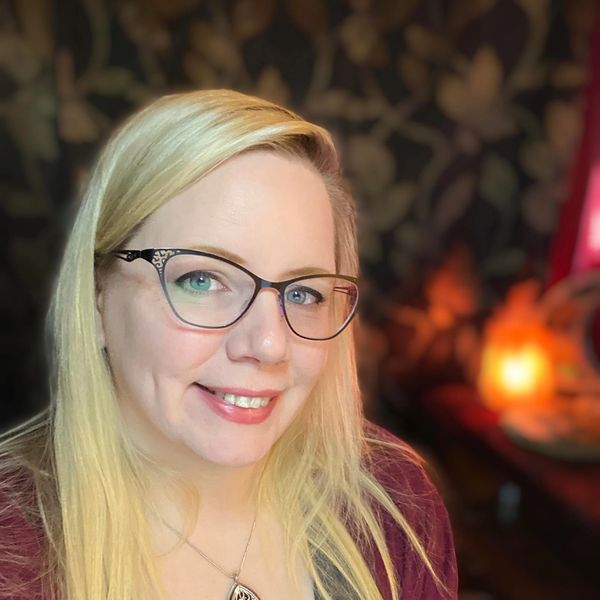 Woman with glasses smiling warmly indoors with soft lighting.