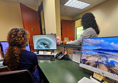 Two women working together in an office with computers and phones.