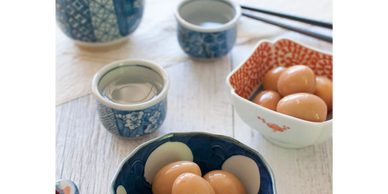 Japanese ceramic bowls with eggs and sake cups on a wooden table.