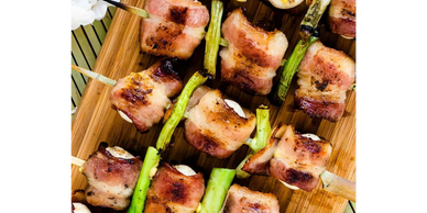 Grilled bacon-wrapped skewers with green onions on a wooden board.