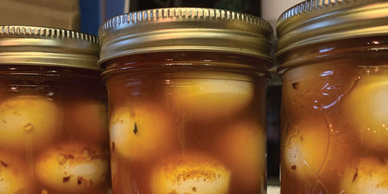 Jars of pickled eggs submerged in a spicy, reddish brine.