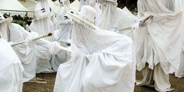 People dressed in white traditional attire playing drums.