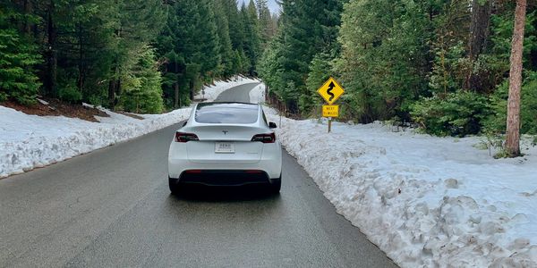 Picture of a Tesla model y driving on the road with snow surrounding it next to a winding road sign