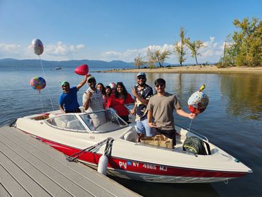 Group of friends celebrating a birthday on a boat by the lake with balloons.