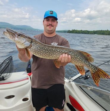 Man proudly holds a large fish on a boat in a lake.