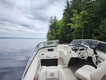 Interior of a white motorboat on calm water near a green forest shore under a cloudy sky.