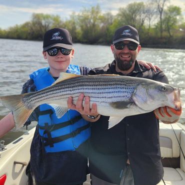 Two men on a boat proudly holding a large striped fish they caught.
