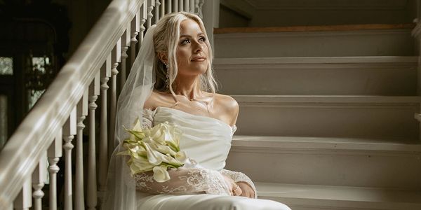 Bride in a white wedding dress holding a bouquet, sitting on stairs.