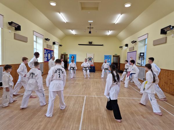 A Taekwondo class practicing in a spacious hall, forming a circle around the instructor.