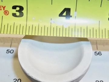 A small white curved object measured against two rulers.