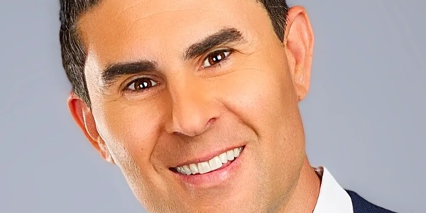 Close-up of a smiling man in a suit with a neutral background.