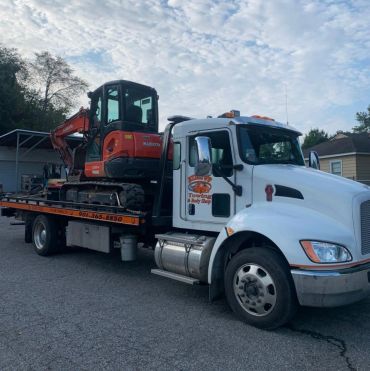 White flatbed truck carrying an orange excavator.