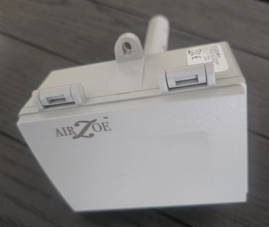 Close-up of an Air Zoe electronic device with clips on a gray surface.