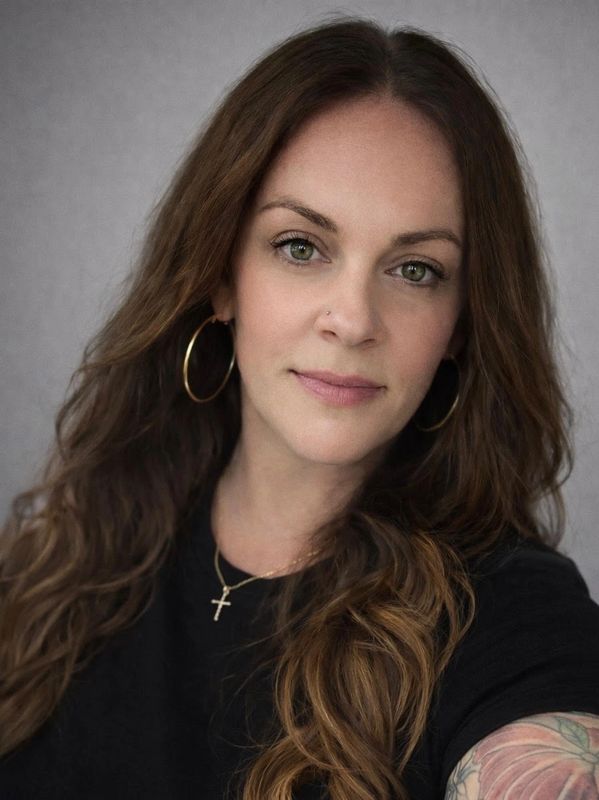 Portrait of a woman with long hair, hoop earrings, and a cross necklace.