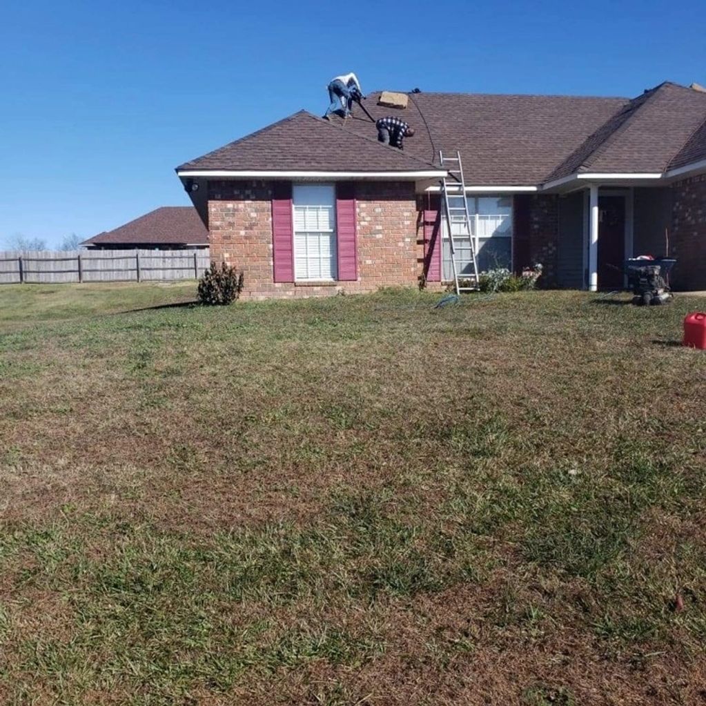 Two roofers laying asphalt shingles on brick house.