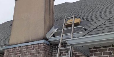 Roofing ladder leaning on an architect shingle roof near a chimney flashing repair