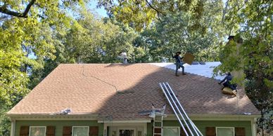 Roofers standing on a house's roof installing new brown shingles