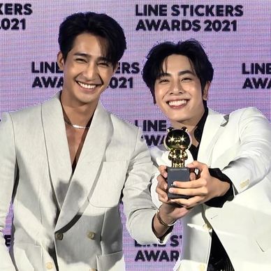 Two men in white suits smiling and holding a trophy at the LINE Stickers Awards 2021.