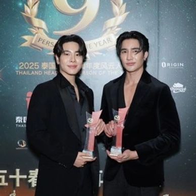 Two men in black suits holding awards at an event.