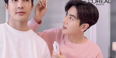 Two men, one applying skincare product to the other's face in a bright setting.
