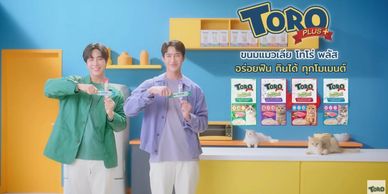 Two men holding Toro Plus snacks in a colorful kitchen setting.