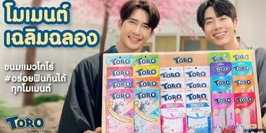 Two men smiling with TORO snack boxes in front of cherry blossom background.