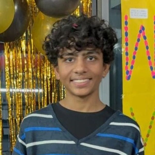 Smiling young person with curly hair at a festive event with balloons and decorations.