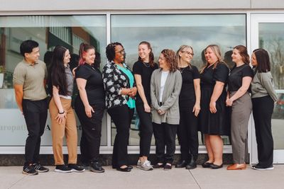 A diverse group of nine people standing and smiling outside a building.