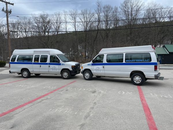Two white Smart Ride LLC vans facing each other in a parking lot.
