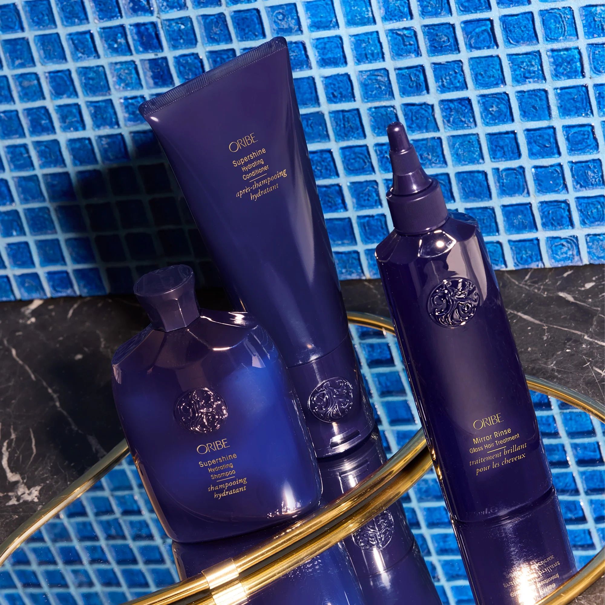 Oribe Supershine blue hair care products on blue tile background.