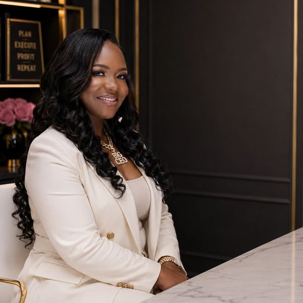 Confident woman in a white suit smiling at a marble table.