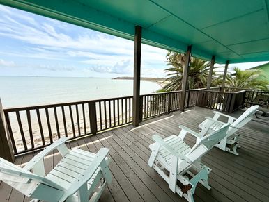 Beachfront deck with white chairs overlooking the sea.