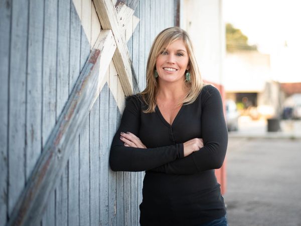 Smiling woman leaning against a wooden wall outdoors.