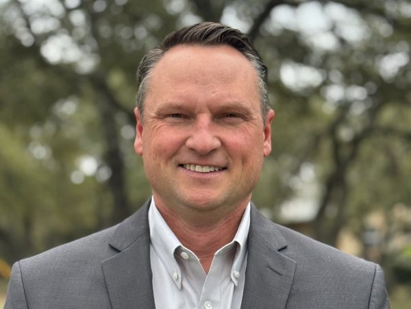 Smiling man in a gray suit outdoors.