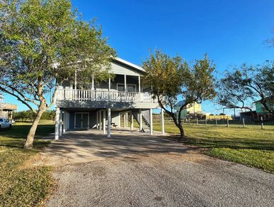 Elevated house with two trees and driveway under a clear blue sky.