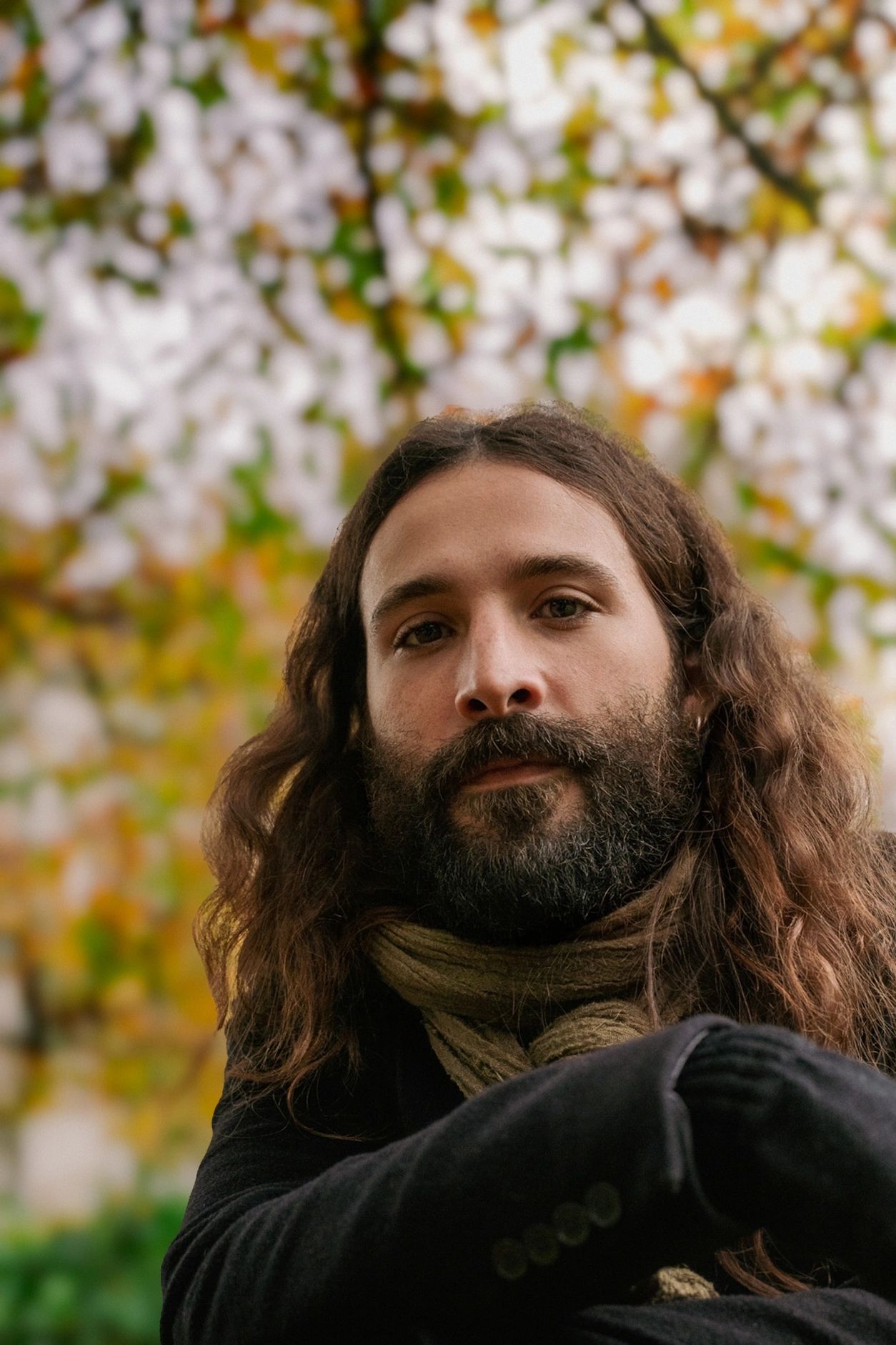 Man with long hair and beard wearing a scarf and black coat.