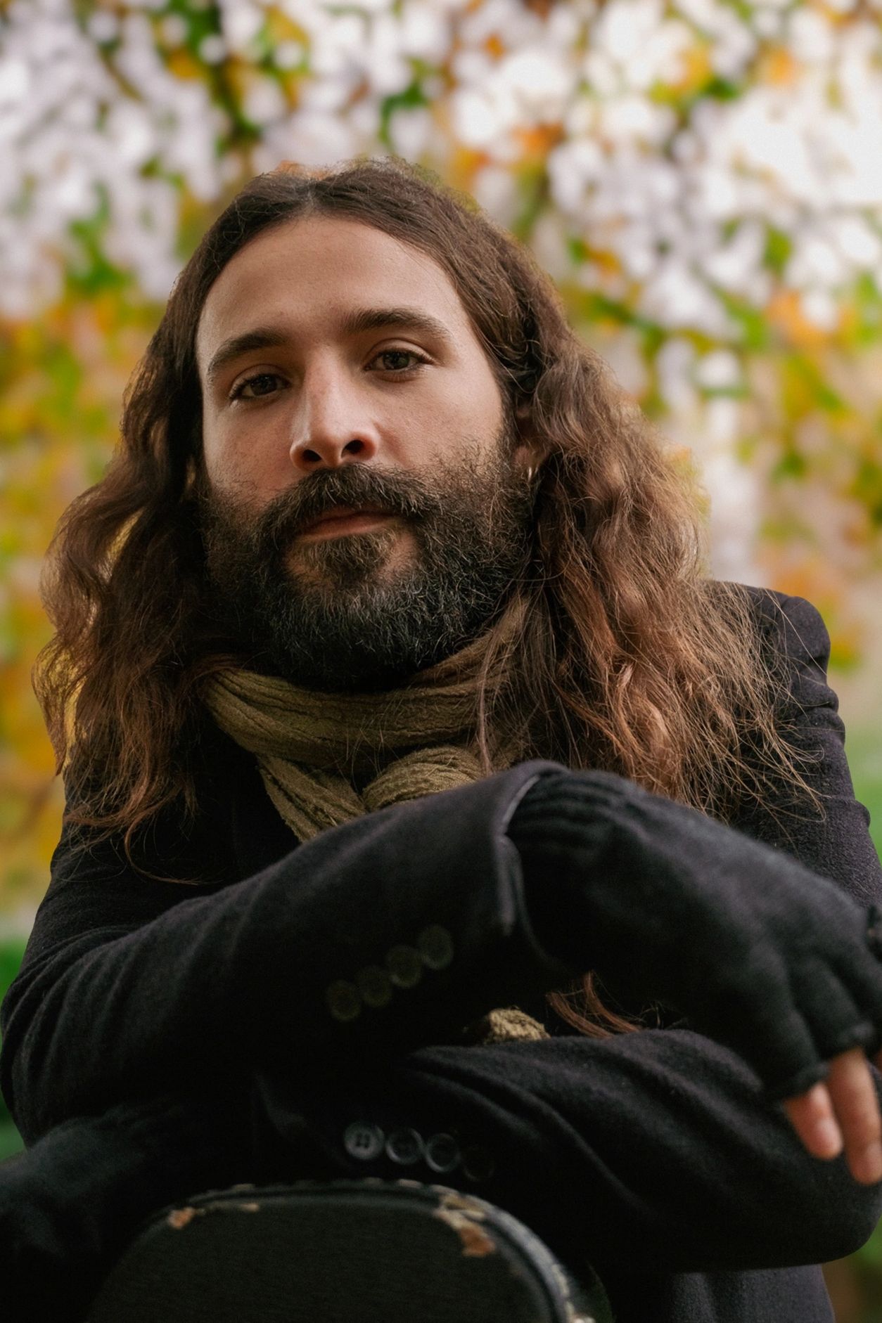 Man with long hair and beard wearing a scarf and black coat.