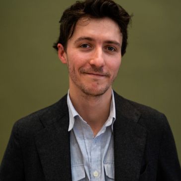 Man in a blazer smiling subtly.