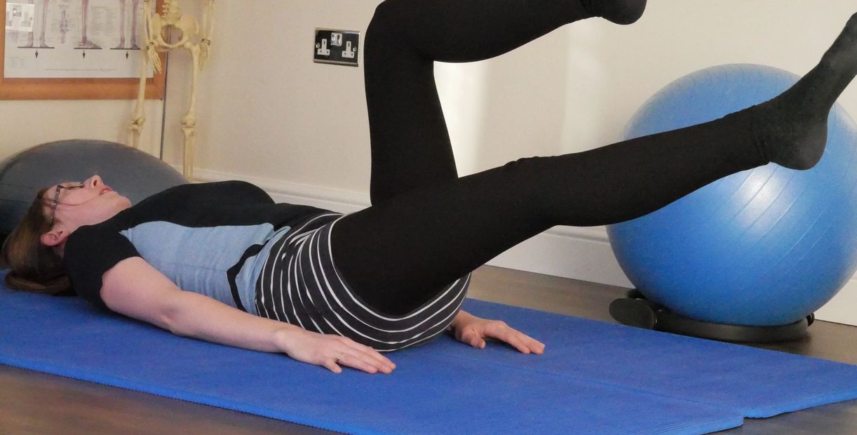 Woman exercising on a blue mat with an exercise ball nearby.